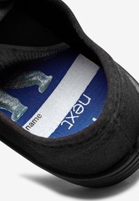 Intérieur de la basket noire montrant une semelle intérieure bleue avec un espace blanc pour écrire un nom et une partie du texte "next".