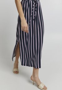 Maksimekko, jossa on tummansinisiä ja vaaleanpunaisia raitoja, sivuventtiilit, nauhavyötärö ja sileä tekstuuri. Yhdistetty vaaleanbeigeihin korokepolkimiin.