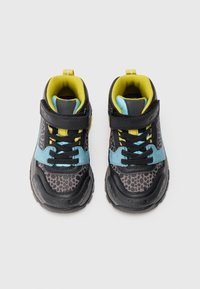 Et par svarte barnesko med gule detaljer, blå aksenter, svarte prikker, snøring og borrelås på en hvit bakgrunn.