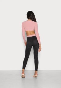 Top corto de manga larga rosa con un corte en la parte posterior. Combinado con jeans negros de cintura alta y sandalias de tacón nude. Textura suave.