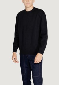 Maglione nero a maglia con un motivo a griglia testurizzato, colletto girocollo e polsini a coste. Abbinato a jeans in denim scuro, con cuciture a contrasto.