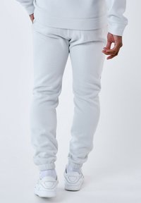 Lichtgrijze joggers van zacht materiaal met elastische boorden. Gecombineerd met witte sneakers en geribbelde witte sokken.