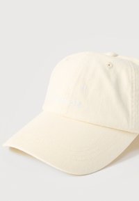 Ανοιχτό μπεζ καπέλο μπέιζμπολ με καμπύλη γείσο, κεντημένο με το κείμενο "CPH STUDIOS" σε λευκό νήμα στο μπροστινό πάνελ.