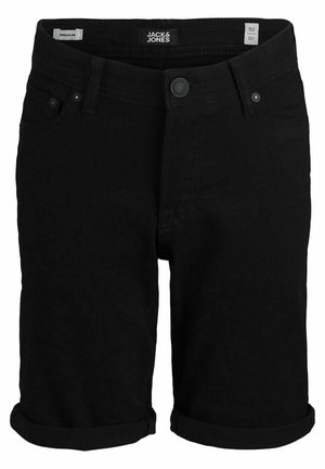 Barn iført en grå t-shirt med mørke bladmønstre, sorte opkrogede shorts og sorte sneakers med hvide såler, stående foran en grå baggrund.