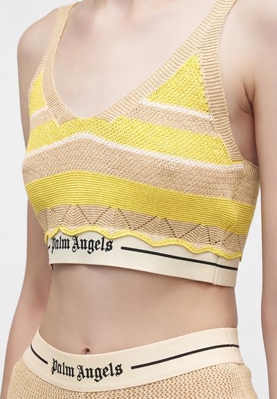 Πλεκτό crop top με κίτρινες, μπεζ και λευκές ρίγες, φορεμένο με αντίστοιχα μπεζ δίχτυ στο κάτω μέρος, και τα δύο με μαύρες λωρίδες με το λογότυπο Palm Angels.