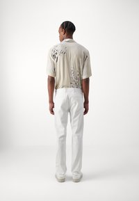 Short-sleeve beige shirt with abstract black print, paired with white straight-leg pants. Minimal design, no visible branding or patterns.