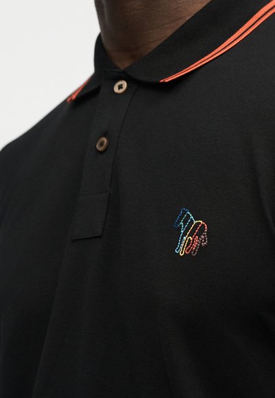 Μαύρο πόλο πουκάμισο με πορτοκαλί ριγέ γιακά και πολύχρωμο κεντημένο λογότυπο στο στήθος, φορεμένο από ένα άτομο.