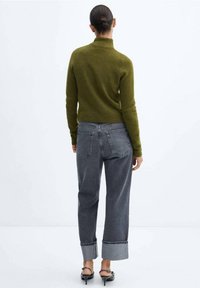 Pull à col roulé vert olive associé à un jean gris taille haute et fuselé, avec des poignets retroussés et deux poches arrière. Design simpliste.