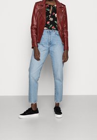 Červená kožená motorkářská bunda přes černou květinovou blůzu, spárovaná s modrými džínami s vysokým pasem a černými teniskami na suchý zip.