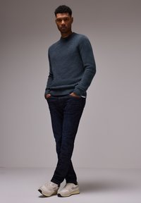 Grå strukturerad stickad tröja, mörkblå jeans och vita sneakers. Tröjan har ribbade muddarna och nederkant, vilket skapar en åtsittande silhuett.