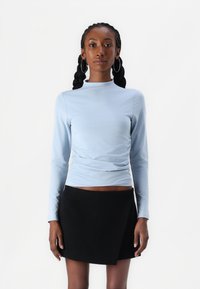 Top azzurro chiaro a maniche lunghe con dettagli arricciati, abbinato a una gonna a portafoglio nera. Texture liscia e design aderente.