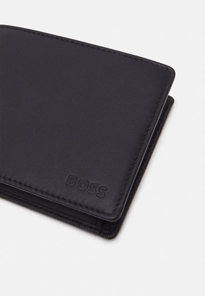 Portefeuille en cuir noir avec une texture lisse, présentant des coutures discrètes et un logo de marque en relief. Compact, de forme rectangulaire.