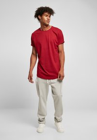 Tricou roșu din bumbac cu mâneci răsucite, combinat cu pantaloni de trening gri, dotati cu buzunare laterale și șnur. Încălțămintea constă în adidași albi.