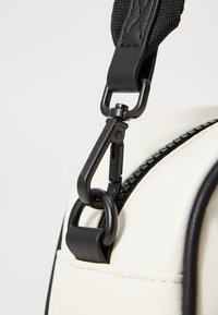 Cream-colored bag with black accents, featuring a textured strap and a black zipper. It has a metal clip for attachment.