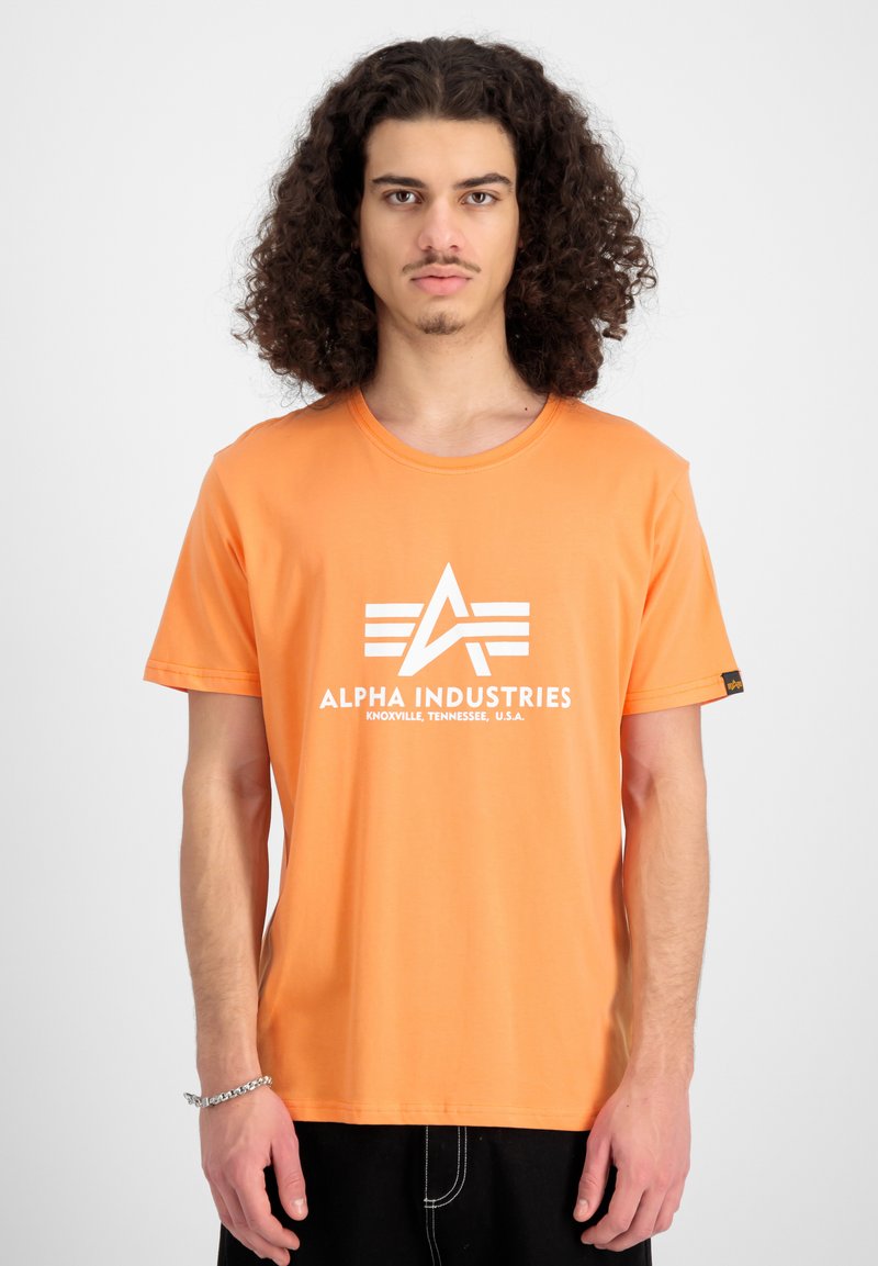 Kurze orange Baumwoll-T-Shirt mit weißem "Alpha Industries"-Logo und Schriftzug. Gerader Schnitt, lässige Passform.