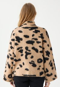 Luipaardprint trui in beige en zwart, geweven stof, oversized pasvorm, wijde mouwen, hoge kraag, zichtbare naaddetails aan de zoom.