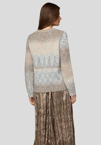 Strickpullover mit einem Farbverlaufsmuster in Beige- und Grautönen; verfügt über einen runden Halsausschnitt und lange Ärmel. Kombiniert mit einem metallischen, plissierten Rock.