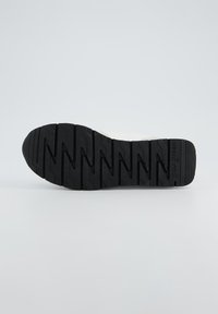 Semelle en caoutchouc noir avec un motif de bande de roulement en zigzag ; surface texturée ; léger talon ; nom de marque en relief "paul green" sur le côté.