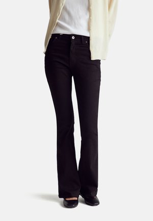 Zwarte flare jeans met een hoge taille, gemaakt van denim. Kenmerken zijn een klassiek vijf-pocket ontwerp, gecombineerd met een lichtgekleurde cardigan en platte schoenen.