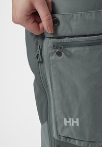 Šedé voděodolné kalhoty s kapsami na zip; texturovaná tkanina a viditelné logo značky. Obsahují zapínání na knoflík a zesílené švy.