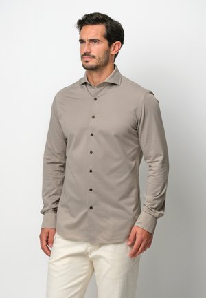 Beige Langarmhemd aus weichem Stoff, mit einem Standardkragen und braunen Knöpfen auf der Vorderseite sowie mit geknöpften Manschetten.