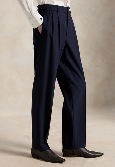 Navy blue wool trousers with front pleats, belt loops, and side pockets, paired with dark leather pointed-toe boots.