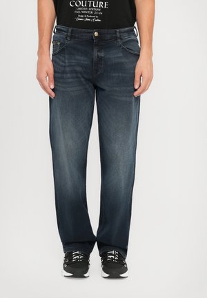 Dark blue denim jeans with a straight cut, featuring two front pockets and a button closure, paired with black sneakers.
