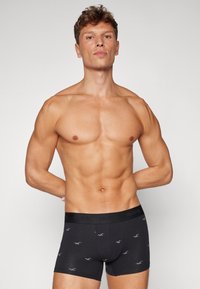 Crne bokserice s diskretnim ponavljajućim uzorkom svijetlosivih logotipa, s širokim elastičnim pojasom na kojem je označeno "HOLLISTER."
