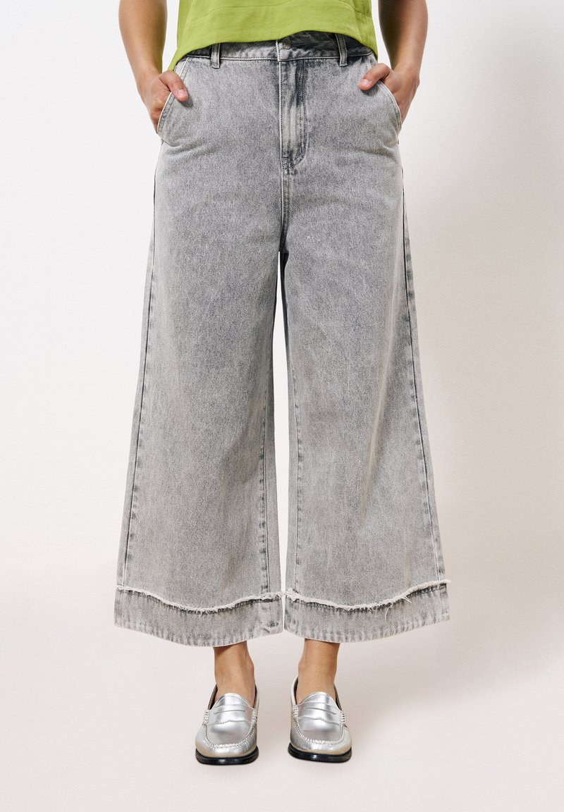 Grijze denim broek met wijde pijpen en rafelige zoom, voorzien van twee zijzakken en een losse pasvorm. Gecombineerd met glanzende zilveren loafers.
