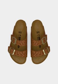 Καφέ σανδάλια με λεοπάρ σχέδιο, δύο ρυθμιζόμενα λουριά, χρυσές αγκράφες και μαξιλαρωτό πέλμα. Επιφάνεια με υφή και επίπεδη σόλα.
