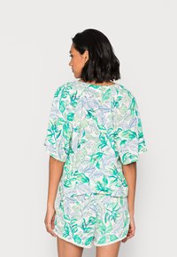 Top com estampado floral, mangas curtas e largas e decote redondo; combinado com calções a condizer com uma bainha em forma de onda e padrões de folhas.