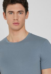 Camiseta gris ajustada con un cuello redondo, mangas cortas y una textura suave. Sin logotipos ni patrones visibles.