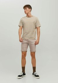 Camiseta de algodón a rayas en beige y crema, combinada con shorts de mezclilla rosa claro. Zapatillas negras con suelas blancas; calcetines marrones.