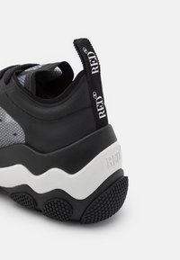 Talon de baskets chunky en noir et blanc avec une semelle texturée, languette de tirage noire affichant le texte "RED" en blanc, et détail de panneau latéral en maille.