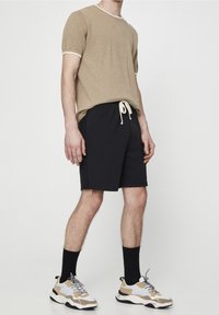 Chemise beige en tricot à manches courtes avec bordure blanche, associée à un short noir à cordons et des baskets beiges avec des accents gris et marron.