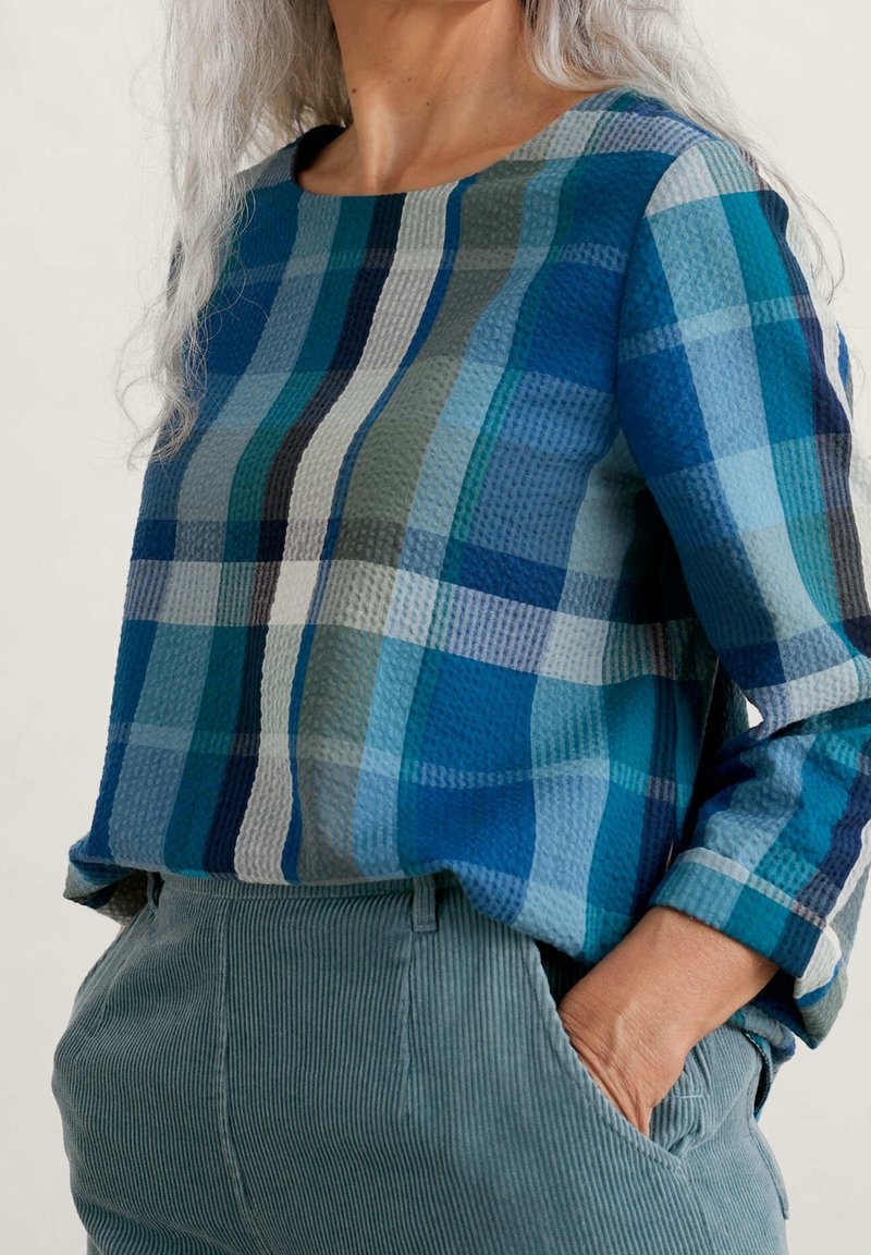 Blue and green checkered long-sleeve top with a textured pattern, paired with light green corduroy pants. Rounded neckline and relaxed fit.