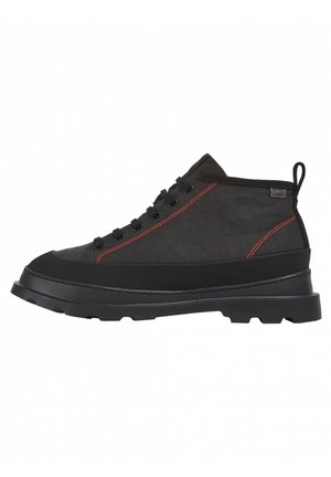 Scarpa alta nera con superficie testurizzata, cuciture rosse e suola in gomma spessa. Presenta occhielli rinforzati e un'etichetta per il sollevamento.