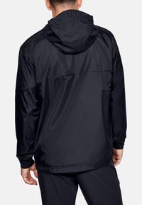 Chaqueta con capucha negra hecha de un material ligero y suave. Presenta un corte relajado, puños elásticos y un dobladillo recto.