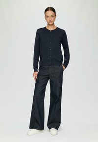 Navy gestrickte Strickjacke mit rundem Halsausschnitt und fünf Knopfverschluss, kombiniert mit weiten, dunklen Jeans und weißen Sneakern.