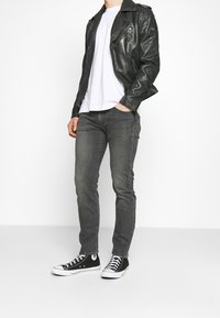 Chaqueta de motorista de cuero negra con herrajes plateados, camiseta blanca, pantalones vaqueros gris ceñidos, y zapatillas Converse negras con suelas blancas.