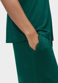 Groene katoenen top met een zak en kantafwerking, gecombineerd met bijpassende broek, die een ontspannen pasvorm en een gladde textuur toont.