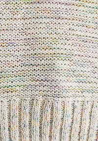Stickad pläd i krämfärgad med flerfärgade knappar. Har en texturerad väv och fransade kanter för extra detaljer.