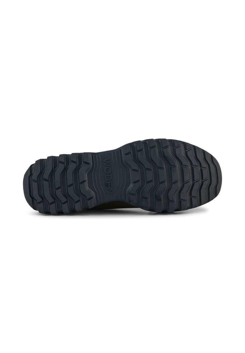 Suela de zapato de goma negra con un patrón de profundidad, con surcos elevados y bordes redondeados, y el nombre de la marca "WODEN" en relieve.