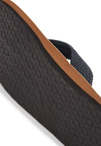 Suola in gomma nera per infradito con superficie testurizzata e presa a motivo. Cinturino in tessuto morbido di colore blu navy con design intrecciato, con bordo chiaro in contrasto.