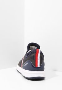 Navy urheilukenkä, jossa on verkkomateriaali päälliosassa, valkoinen pohja ja punavalkoiset raidat. "POLO"-logo näkyy sivussa.