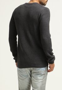 Donkergrijze geribbelde trui met lange mouwen, ronde hals en gestructureerde stof, gecombineerd met lichtblauwe jeans, gezien vanaf de achterkant.