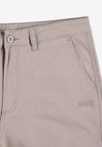 Beżowe spodnie bawełniane z zamkiem i zapięciem na guzik, kieszenią boczną oraz subtelnym haftem marki z przodu. Gładka struktura.