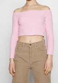 Růžový top bez ramínek, zkrácený s dlouhými rukávy v texturovaném materiálu, spárovaný s vysokými béžovými kordovými kalhotami.