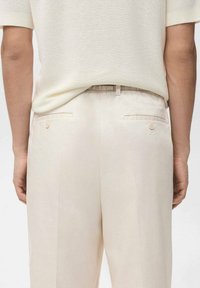 Beżowe spodnie o gładkiej fakturze, z luźnym krojem, tylnymi kieszeniami zapinanymi na guziki oraz pasem zaprojektowanym dla komfortu.