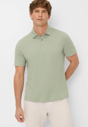 Hellgrünes Polohemd mit Kragen, kurzen Ärmeln, einer Dreiknopf-Leiste und einer glatten Stoffstruktur. Im Outfit kombiniert mit hellen Hosen.